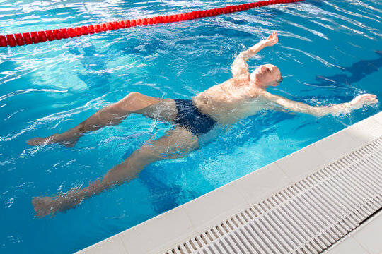 A 70-year-old pensioner is resting, swimming, recovering in the pool with clear and blue water in the hotel.