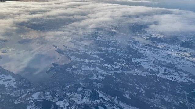 Skimming above clouds over Trondheim fjord with bright golden sun contrast with blue snowy ground and the sky reflected on the water, panning shot right to left