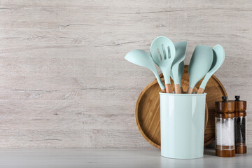 Holder with kitchen utensils, spice shakers and serving boards on white wooden table. Space for text