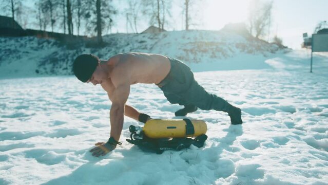 Young muscular man exercising in a winter park and doing exercise plank by moving a can of compressed air from side to side