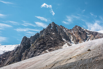 Scenic mountain landscape with glacier under sharp rocks in sunlight. Awesome landscape with glacial tongue and rocky pinnacle in sunshine. Beautiful view to snow mountains at very high altitude.