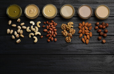 Jars with butters made of different nuts and ingredients on black wooden table, flat lay. Space for text