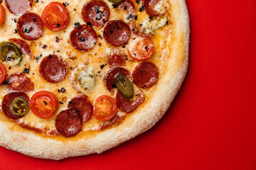 Pizza with smoked sausage, cherry tomatoes, dried chilli, jalapeno peppers and mozzarella. Red background. Top view. Copy space
