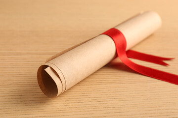 Graduation diploma tied with red ribbon on wooden table, closeup