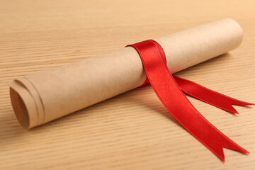 Graduation diploma tied with red ribbon on wooden table, closeup