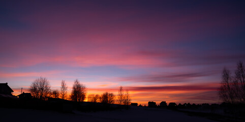 Silhouettes of houses and trees against the bright evening sky. The bright glow of sunset. Pink dawn. Cloudy weather. Scenic natural background. Wallpaper. Scenic view. Twilight in the countryside