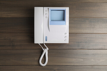 Modern intercom system with handset on wooden background, top view