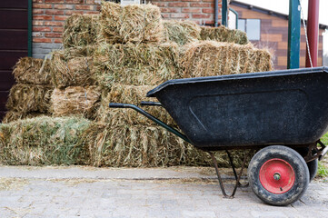 Hay stacks and wheelbarrow in front of animal stable entrance