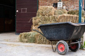 Hay stacks and wheelbarrow in front of animal stable entrance