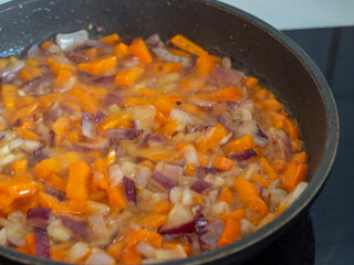 Onions and carrots are fried in a pan.