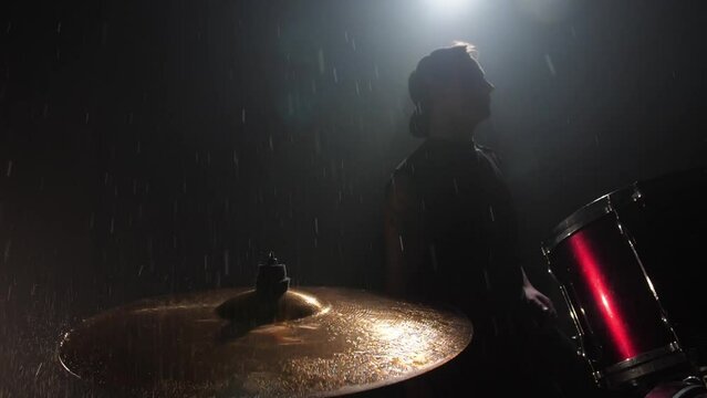 The drummer hits the wet drum cymbal with his drumstick and the water splashes in slow motion. In the recording studio of musical instruments. Knocks and beats of rock music band.
