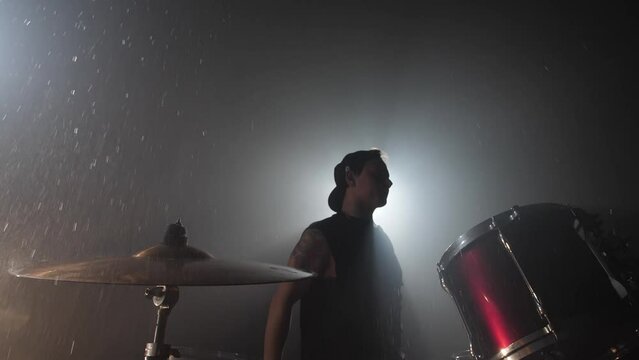 The Drummer's silhouette beats a drumstick on a wet drum cymbal, water flying out in slow motion. A recording studio of musical instruments filled with smoke