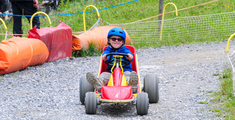 young boy rolling down hill in a go kart in the french alps at super devoluy ,holiday activity ,ski resort in summer . - obrazy, fototapety, plakaty