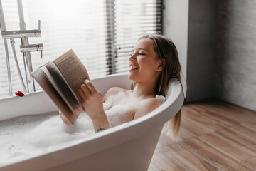 Happy woman lying in foamy bath, reading book in relaxing atmosphere, enjoying interesting story in...