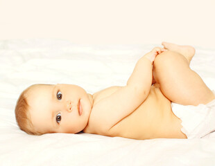 Portrait of cute baby in diapers lying on white bed at home