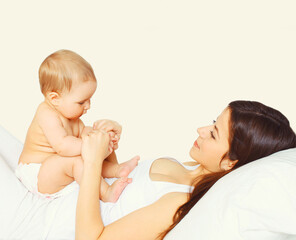 Portrait of happy young mother and cute baby lying on the bed at home together on white background