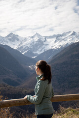Fototapeta na wymiar young woman leaning on a wooden fence enjoying a beautiful snowy mountains views