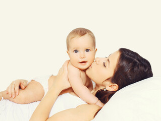 Portrait of happy young mother and cute baby lying on the bed at home together on white background