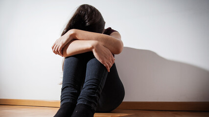 Portrait of sad depressed young woman sitting on floor in empty room at home.