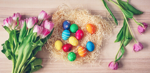 Colorful easter eggs in nest and tulips on the wooden background.