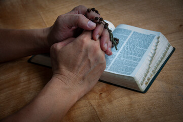 Hand holding Rosary on a Holy Bible praying. Prayer concept.
