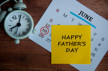 Happy father's day text on yellow sticky note with calendar and white alarm clock background.