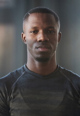 Fototapeta premium Vertical medium close-up portrait of confident young African American man wearing dark gray T-shirt standing indoors looking at camera