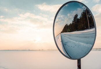 Convex mirror reflecting winter road. Snowy landscape in the background.