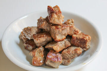 Cooked diced beef, on a white small plate, isolated on white background