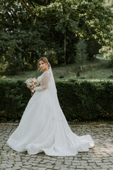 Fototapeta na wymiar Gorgeous stylish bride in vintage white dress walking in the park
