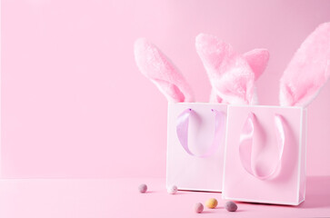 The concept of Easter shopping. Paper colored bags for goods with bunny ears on a pink background