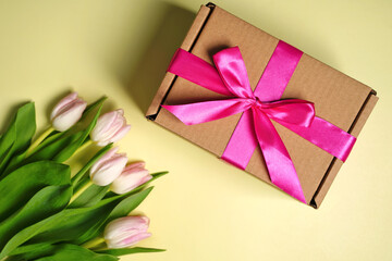 Decorative gift box with pink ribbon and tulips on light background