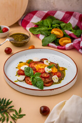 Caprese. Italian caprese salad with cherry tomatoes, mozzarella cheese, basil and pesto on a plate on a beige background. Traditional Italian food. Vegetarian dish. Healthy salad. Italian cuisine.