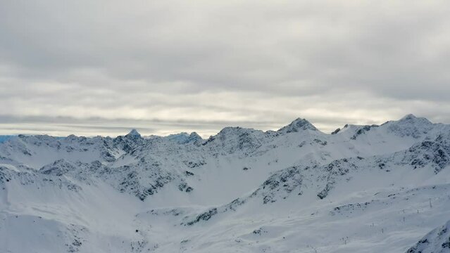 Aerial trucking shot of the majestic alpine peaks in the famous Swiss ski resort Arosa covered in snow on cloudy weather