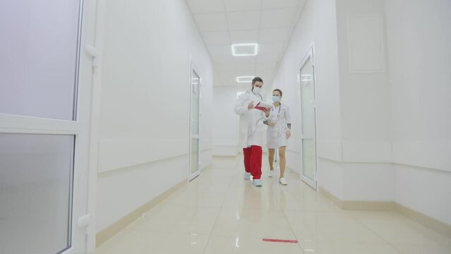 Doctors in antiviral protection are walking along the bright hospital corridors. Doctors walk along the bright modern corridors of the hospital