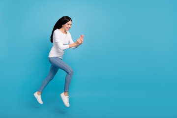 Fototapeta na wymiar Full length body size view of attractive cheerful active girl jumping using device blog isolated on bright blue color background