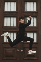 Front image of a teenager dressed in black jumped up and down a building.