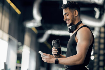 Fitness App. Smiling Arab Sporty Man Using Smartphone While Standing In Gym