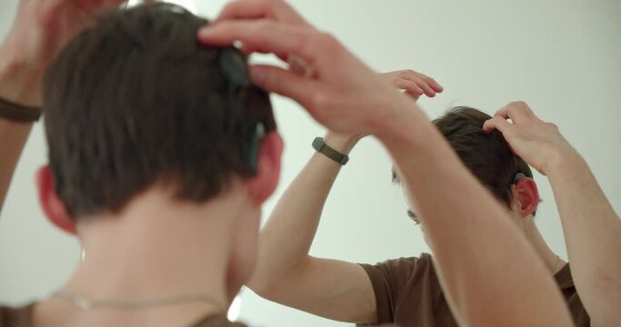 a young man puts on a cochlear implant, a hearing aid, looking at himself in the mirror
