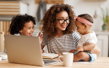 Young happy african american woman freelancer working remotely from home with two little kids