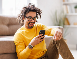 Cheerful black male using smartphone near sofa