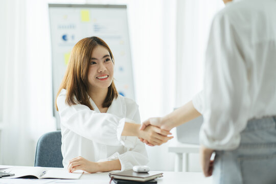 Pretty asian business woman shaking hands with business woman in her office during meeting.