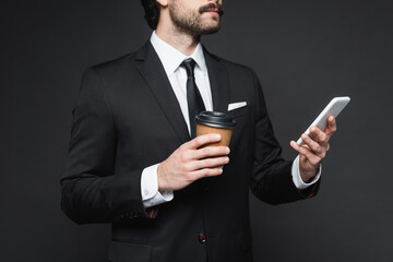 cropped view of businessman with mustache holding paper cup and smartphone on dark grey.