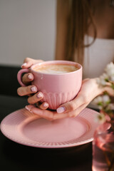 Woman's hand holds a pink mug with coffee, breakfast in a coffee shop