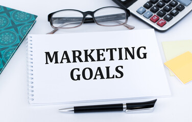 Marketing goals text on a notepad on a table next to a pen, glasses, calculator
