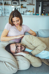 A sweet couple in love on a weekend morning. They hug on the sofa in the house, in casual clothes. Behind them is the kitchen, the interior is modern and comfortable