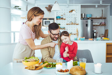Mom, dad and daughter cook in the kitchen. The concept of a happy family. A handsome man, attractive young women and their sweet daughter eat salad and bread together. Healthy way of living.