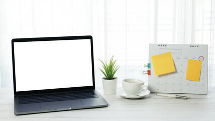 Blank white screen desktop laptop computer with coffee cup and stationery on vintage wooden table...