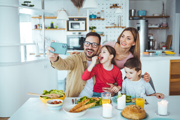 A young father and mother and child are in the kitchen, preparing a healthy meal together and taking selfies. The modern family enjoys together. The concept of happiness and love