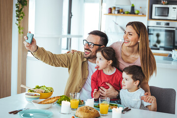 Bonding and lifestyle. Portrait of a family taking selfies together at home indoors. Happy parents posing with their children and smiling at the camera, sitting on the couch in the living room.
